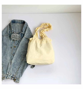 Detail of light yellow pleated tote bag with ruffled straps on white background