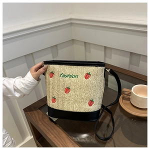 Detail of straw bucket bag with red strawberry embroidery and black leather strap