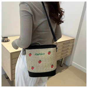 Close-up of straw bucket bag featuring embroidered strawberries and black leather accents