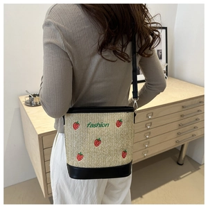 Detail of straw bucket bag with red strawberry embroidery and fashion logo on model