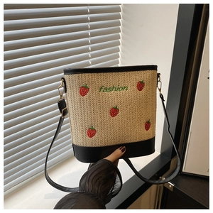Detail of straw bucket bag featuring embroidered strawberry patterns and black leather trim
