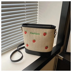 Detail view of woven straw bucket bag featuring embroidered red strawberries and green text