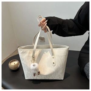 Detail of off-white tote bag featuring subtle texture and stylish plush charm accessory