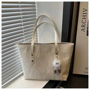 Detail of off-white tote bag with pleated texture and cute plush charm in natural light