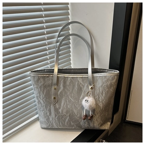 Detail of silver tote bag with metallic texture and cute white plush doll keychain charm