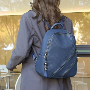 Detail of dark blue plaid embossed backpack featuring diagonal zippers and metal charm
