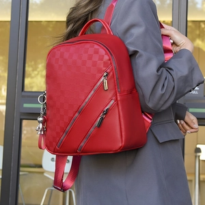 Detail of red quilted backpack with checkered pattern and metallic pendant charm