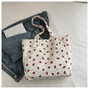Flat lay of white corduroy tote bag with strawberry print and blue jeans lifestyle setting