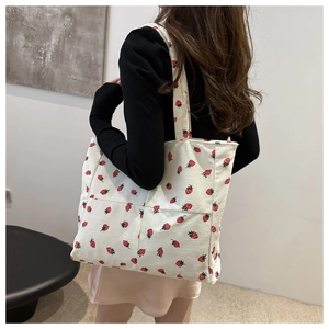Detail view of corduroy tote bag with strawberry embroidery in a minimalist interior setting