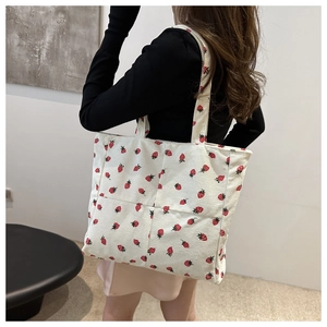 Model wearing a large corduroy tote bag with red strawberry print in a minimal setting