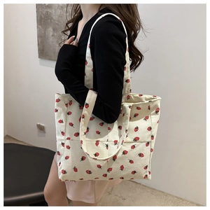 Detail of white corduroy tote bag with strawberry print worn by model for daily use