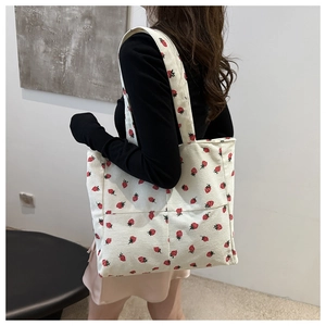 Detailed close-up of white corduroy tote bag with red strawberry pattern and wide strap