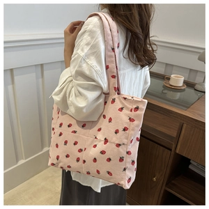 Detail of pink corduroy tote bag with strawberry prints worn over the shoulder