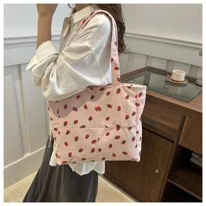 Detail of pink corduroy tote bag featuring an all-over strawberry print and soft handle