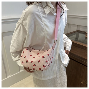 Close-up of pink corduroy shoulder bag with strawberry prints and golden metal buckles