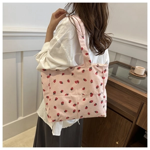 Close-up of pink corduroy tote bag with strawberry print worn by a model in a cozy setting