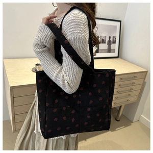 Detail of black corduroy tote bag with strawberry print shown on model's shoulder
