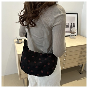 Detailed strawberry embroidery on black corduroy shoulder bag styled in casual setting