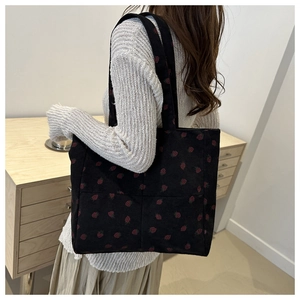 Detail of black corduroy tote bag with strawberry embroidery worn by a model