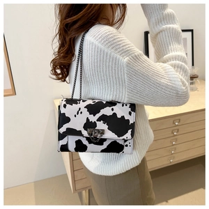 Detail shot of a black and white cow print shoulder bag with metal chain strap on model