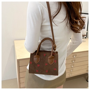 Detail of strawberry print corduroy small square bag worn over the shoulder