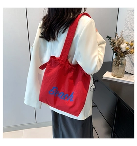 Detail of red canvas tote bag with blue Beach lettering worn on a shoulder