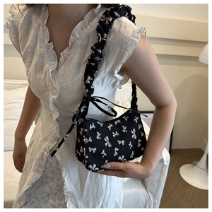 Detail of black floral shoulder bag with white bow patterns and ruched strap design