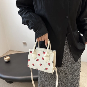 Beige corduroy crossbody bag with embroidered strawberry patterns and leather handle
