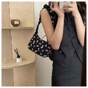 Detail of black crossbody bag with white bow patterns and pleated strap on a model