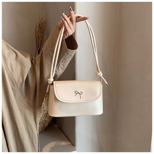 Detail of cream PU leather bucket bag featuring a metallic bow and knotted rope shoulder strap