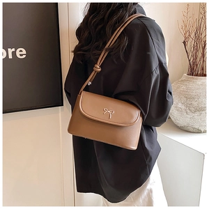 Brown crossbody bag with gold bow detail and knotted shoulder strap shown on model