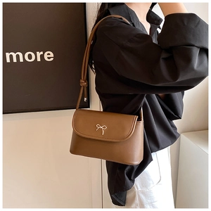 Detail of a dark brown shoulder bag featuring a gold metal bow on smooth leather