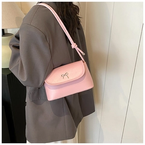 Detail of pink shoulder bag featuring a small gold bow clasp and adjustable strap