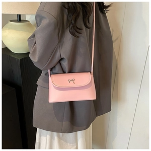 Detail view of pink underarm bucket bag with golden bow clasp worn by a model