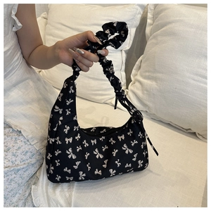 Detail of a black underarm bag with white bow patterns and a ruched handle on white bedding
