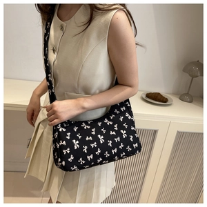 Floral print shoulder bag with bow patterns and adjustable strap shown on model