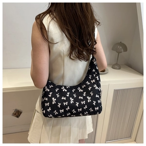 Close-up of a black hobo bag with white bow patterns worn by a model in a room