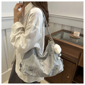 Detail of silver metallic hobo bag featuring butterfly charms and a white plush pompom