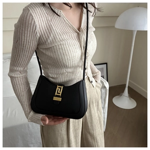 Detail of a black leather shoulder bag with a gold geometric clasp shown on a model