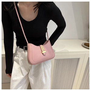 Close-up of pink crescent shoulder bag with golden geometric clasp detail on light background