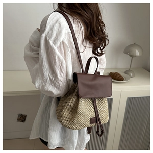 Detailed view of woven straw backpack with brown leather trim and drawstring closure