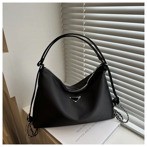 Detail of black nylon shoulder bag with silver triangular metal logo on white books