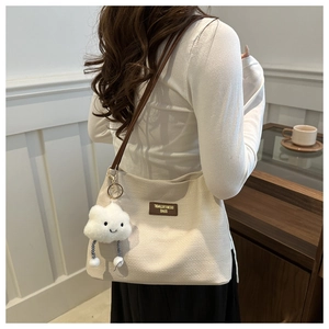 Detail of waffle textured tote bag with leather strap and plush cloud charm accessory