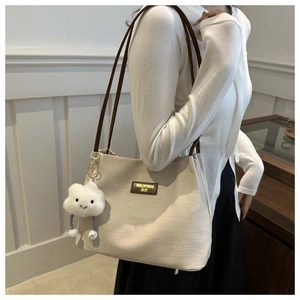 Detail of beige woven tote bag with dark brown strap and plush cloud charm accessory