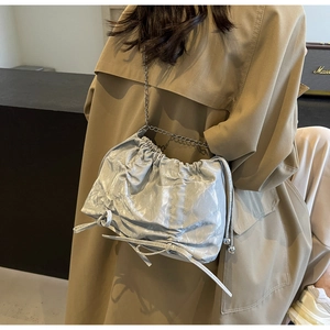 Detail of silver pleated tote bag with chain strap styled with a trench coat