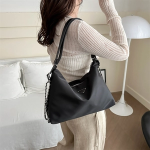 Chic black nylon tote bag with metal chain strap and logo plaque on a female model