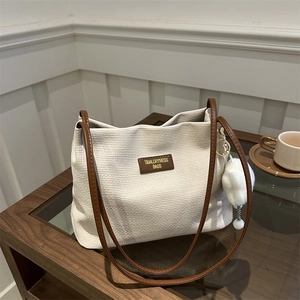Chic woven tote bag in off-white with brown leather straps and plush ball accessory