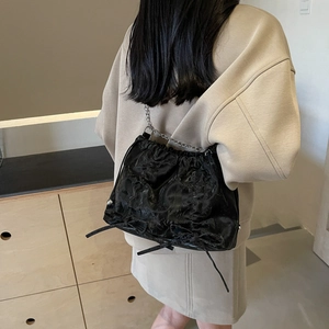 Large black pleated tote bag with silver chain strap and bow details in a minimalist setting