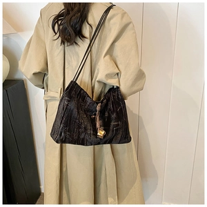 Detail of black pleated fabric tote bag with elegant golden knot charm on shoulder