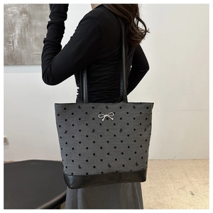 Side view of gray canvas polka dot tote bag with metal bow detail worn by a model